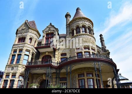 Blick nach oben auf den reich verzierten viktorianischen Stil 1892 Bishops Palace in Galveston, Texas. Die Villa schafft ein dramatisches Profil vor einem hellblauen Himmel. Stockfoto