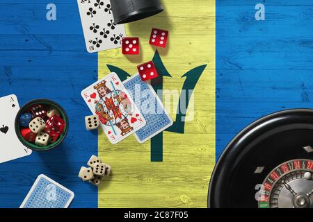 Barbados Casino Thema. Asse im Pokerspiel, Karten und Chips auf rotem Tisch mit nationaler Holzfahne Hintergrund. Glücksspiel und Wetten. Stockfoto