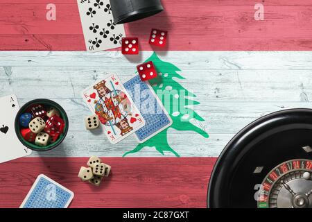 Libanon Casino Thema. Asse im Pokerspiel, Karten und Chips auf rotem Tisch mit nationaler Holzfahne Hintergrund. Glücksspiel und Wetten. Stockfoto