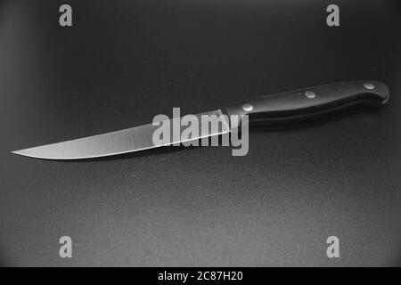 Isoliertes silbernes Steakmesser mit schwarzem Griff auf schwarzem Hintergrund Stockfoto