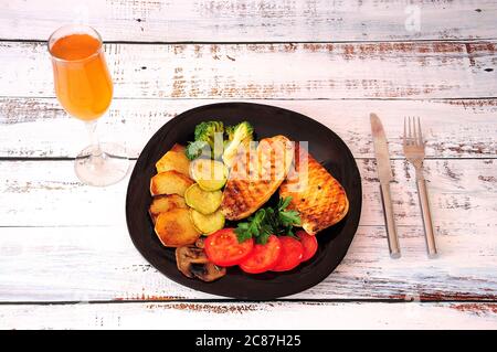 Ein großes Glas Wein und ein köstlicher Teller, zwei Hühnersteine mit Tomaten, Bratkartoffeln, Zucchini, Pilzen und Brokkoli. Nahaufnahme. Stockfoto
