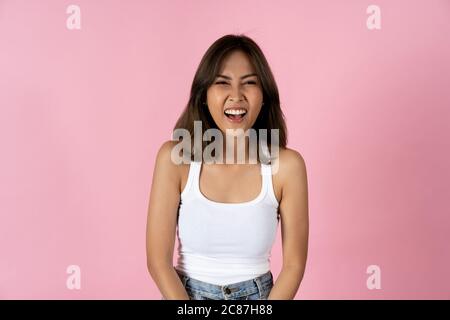 Fröhliche junge Frau, die vor einem einfachen rosa Hintergrund auf die Kamera schaut Stockfoto