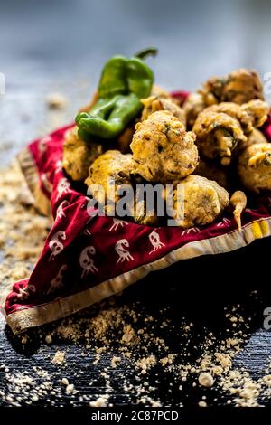 Nahaufnahme von frisch gebratenem Methi Pakora in einem Behälter auf einer schwarzen Oberfläche zusammen mit einigen Gewürzen und einem Kichererbsenmehl auf der Oberfläche verteilt. Methi Stockfoto