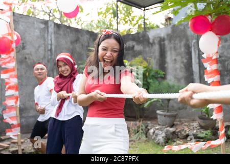 Junge asiatische Frau in rot schreien, als sie versuchte, das Seil hart während des Tauziehen-Wettbewerbs auf Indonesiens Unabhängigkeitstag Feiern zu ziehen Stockfoto