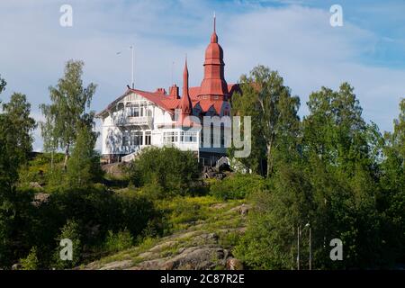 Auf einer Anhöhe auf einer der vielen Inseln thront ein altes, ikonisches, weißes viktorianisches Herrenhaus mit einem Metalldach. Kreuzfahrt auf dem Finnischen Meerbusen in der Nähe von Helsinki. Stockfoto