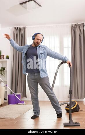 Fröhlicher Mann, der Musik auf Kopfhörern hört und den Boden mit Staubsauger reinigt. Stockfoto