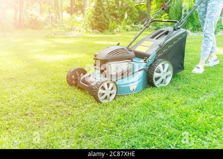 Schönes Mädchen schneidet den Rasen. Rasenmähen. Schöne Frau Rasenmäher auf grünem Gras. Rasenmäher. Mähgärtner Pflege Arbeitswerkzeug. Nahaufnahme Stockfoto