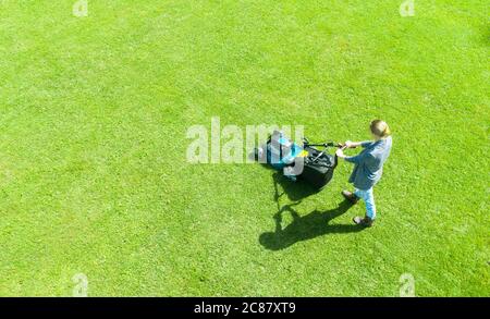 Schöne Mädchen, schneidet den Rasen. Mähen rasen. Luftaufnahme schöne Frau Rasenmäher auf grünem Gras. Mähwerk Gras. Mähen Gärtner Care arbeiten Stockfoto