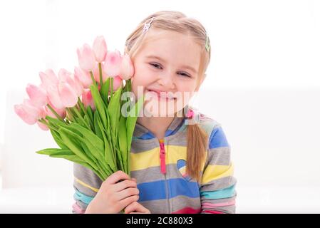 Fröhliche schöne kleine Mädchen mit einem Arm voller bunten Blumen, auf weißem Hintergrund Stockfoto