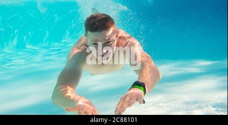 Junger attraktiver Mann, der im Schwimmpoll unter Wasser schwimmend ist Stockfoto