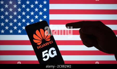 Huawei-Logo auf Smartphone Silhouette und Hand darauf zeigend. Die unscharfe US-Flagge auf dem Hintergrundbildschirm. KEINE MONTAGE, echtes Foto. Stockfoto