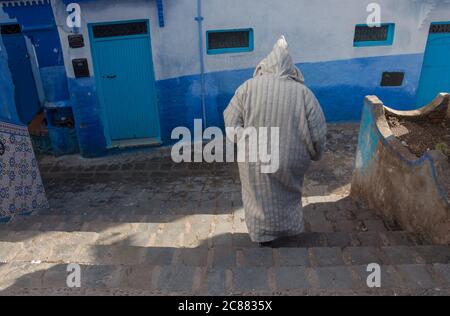 Ein alter Mann, der die traditionelle marokkanische Jillaba trägt, geht durch die blauen Straßen von Chefchaouen, der blauen Stadt in Marokko. Reiseziele Stockfoto