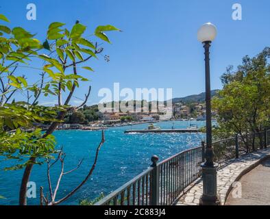 Kai des Dorfes Kassiopi mit Lampe und Bäumen mit Blick auf den Hafen und bunte Häuser, Kassiopi ist touristisches Dorf im Norden der Insel Stockfoto