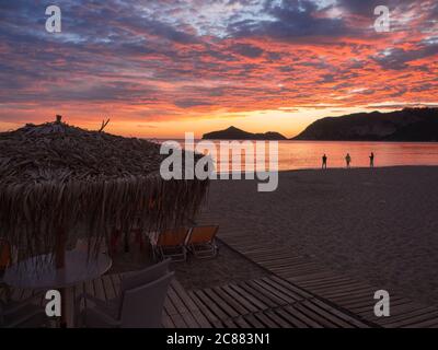 Wunderschöne blau rosa orange Wolken nach Sonnenuntergang am Agios Georgios Pagon Strand auf Korfu Insel, Griechenland mit Sonnenschirmen leere Sonnenliegen und sillhouttes Stockfoto