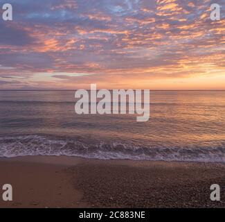 Wunderschöne pastellrosa orange und goldene Sonnenuntergangswolken und Wellen am Ufer des Agios Georgios Pagon Strandes auf der Insel Korfu, Griechenland Stockfoto