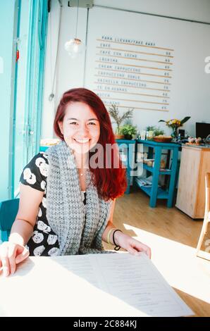 Eine brasilianische Rotschopf Frau in ihren 20ern lächelt, während sie in einem türkisfarbenen Café sitzt, das kürzlich in San Telmo Nachbarschaft eröffnet wurde. Stockfoto