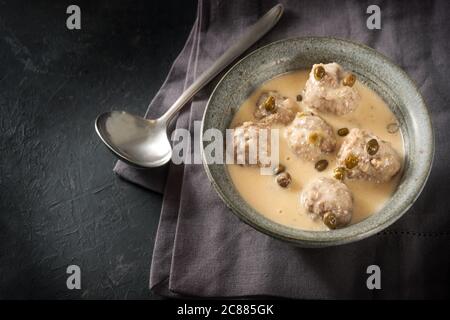 Gekochte Fleischbällchen in weißer Bechamelsauce mit Kapern, Königsberger Klopse genannt, traditionelles polnisches und deutsches Gericht in einer Schüssel auf einem dunkelgrauen Backgro Stockfoto