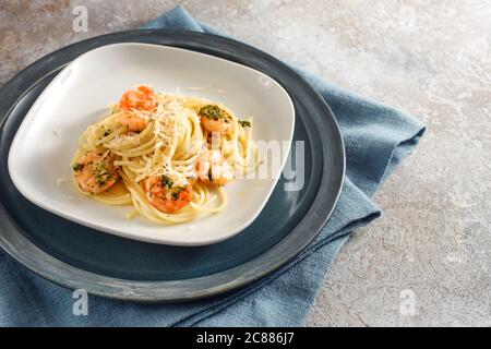 Spaghetti-Gericht mit Garnelen, Petersilie und Knoblauch auf einem Teller, mediterrane Meeresfrüchte, blaue Serviette und rustikalen grauen Hintergrund mit Kopierraum, ausgewählt für Stockfoto