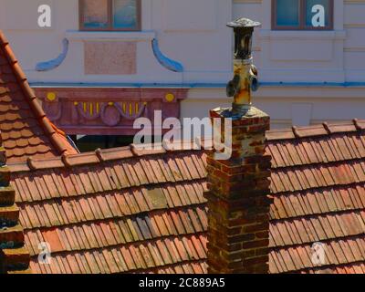 Alte Ziegel und Gusseisen Kamin über hellbraunen Lehm Fliesen Dachrücken und verschwommen eklektischen Stuckfassade Hintergrund. Alte Stadt Architektur Konzept Stockfoto