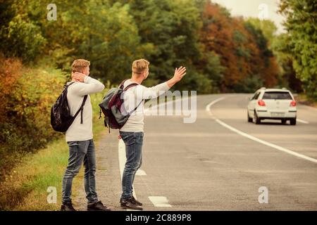 Neue Leute zu treffen. Auf der Suche nach transportieren. Zwillinge zu Fuß entlang der Straße. stop Auto mit "Daumen hoch" Geste. per Anhalter fahren und anhalten Auto mit Daumen nach oben Geste auf die Landschaft. Auf der Straße. Genießen Sommer wandern. Stockfoto