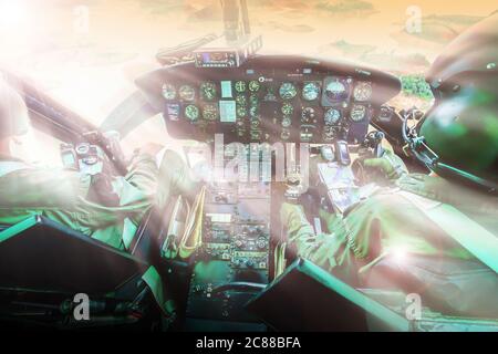 Military helicopter cockpit with two pilots flying against sunset over a lake and mountain range. Focus on control panel. Stockfoto