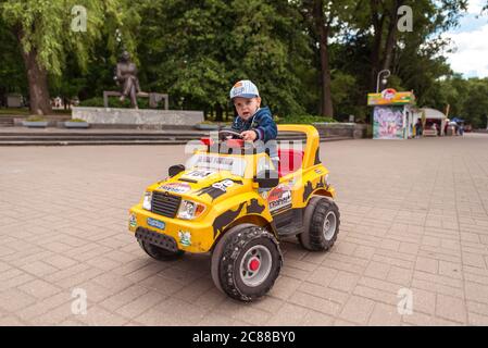 Minsk / Weißrussland - 5. Juni 2019: Portrait eines blonden Jungen in der Mütze, der im Gorki Park ein gelbes Spielzeugauto fährt Stockfoto