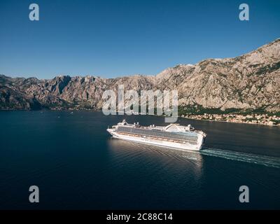 Luftaufnahme von einer Drohne - ein großer Kreuzfahrtschiff schwimmt in der Bucht in der Nähe der felsigen Berge. Stockfoto