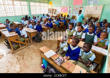 Schulkinder in Uniform saßen an Holztischen und hörten während des Unterrichts ihrem Lehrer in Nairobi, Kenia, zu Stockfoto