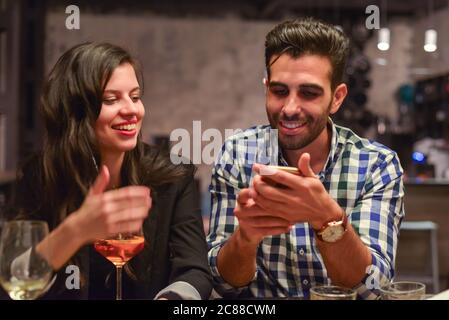 Minsk / Weißrussland - 5. Juni 2019: Junge Paar von lateinischen Mann und weißrussische Frau mit ihrem Telefon und im Gespräch in der modernen Bar Stockfoto