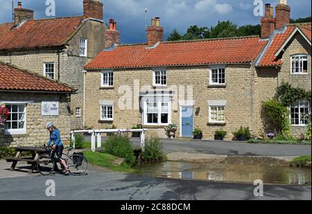 Junge Frau auf dem Fahrrad in dem Dorf Hovingham, Ryedale, North Yorkshire, England Stockfoto