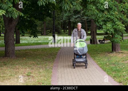 Minsk / Weißrussland - 5. Juni 2019: Erwachsene Mann schiebt Baby-Karren in Park mit viel Grün Stockfoto