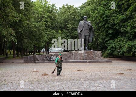 Minsk / Weißrussland - 5. Juni 2019: Kehrerin mit Strohbeben, die trockene Blätter vor der Skulptur im Park reinigt Stockfoto