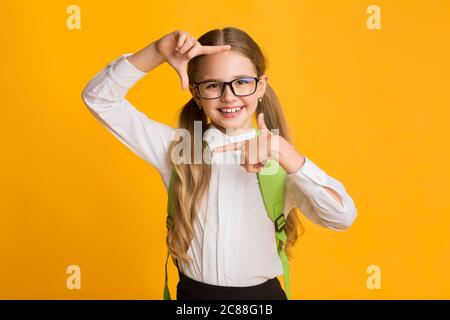 Fröhlich Schulmädchen Blick Auf Kamera Durch Finger Frame, Studio Shot Stockfoto