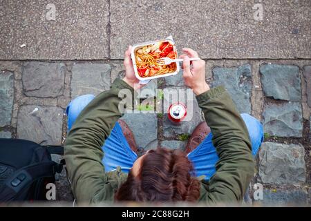 Blick von oben auf einen männlichen Touristen, der auf der Straße am Camden Market in London chinesisches Essen zum Mitnehmen isst Stockfoto