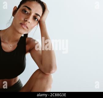 Fitness-Frau sitzt auf weißem Hintergrund mit der Hand auf dem Kopf. Müde Frau, die sich nach dem Workout entspannt und in die Kamera blickt. Stockfoto