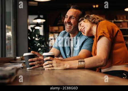Schöne Frau, die ihren Kopf auf die Schulter des Mannes setzt, während sie in einem Café sitzt. Lächelndes Paar im Café. Stockfoto