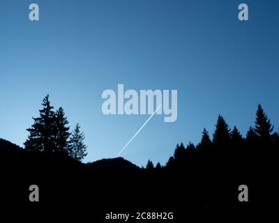 Silhouette Baumlinie und Hügel gegen frühen Morgen blauen Himmel Hintergrund. Weiße Dampfspuren steigen hoch. Bewegung in Stille. Stockfoto