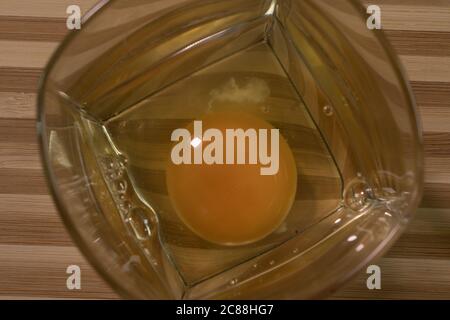 Rohes Ei in einem Glasbecher. Auf einem Holzbrett Stockfoto