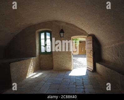 Mittelalterliches Haus mit Tonnengewölbe offene Tür Laterne grünes Fenster Und Blick auf den Hof gelbe Steinmauern und Pflastersteinpflaster Stockfoto