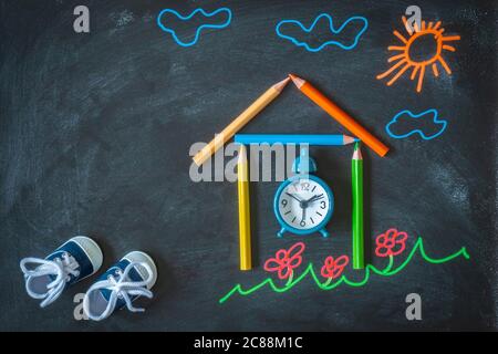 Zurück zum Schulhintergrund mit farbiger Kreidezeichnung, kleinen Sneakers, Schule aus Bleistiften und Wecker. Flaches Lay der Zeichnung auf der Tafel Stockfoto