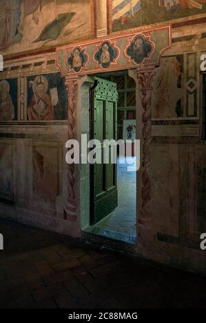 Kapellentür im Castello dei Conti Guidi, einer 1274 gegründeten Burg in Poppi, Toskana, Italien. Die Tür öffnet sich unter einem Fresko aus Gospel-Szenen von Taddeo Gaddi (ca. 1290-1366) und wird flankiert von bemalten architektonischen Dekorationen und einem Frieze von Heiligen von anderen Künstlern. Gaddi galt als die talentierteste Schülerin des florentinischen Malers Giotto di Bondone (ca. 1267-1337). Stockfoto