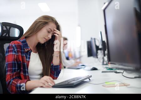 Müde Casual Business Frau, die eine Pause während der Arbeit auf Desktop-Computer in modernen offenen Plan Startup-Büro Innendeadline Stress-Konzept Stockfoto