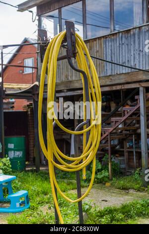 Gelber Gartenschlauch, der an einem Metallmast im Hinterhof hängt Stockfoto