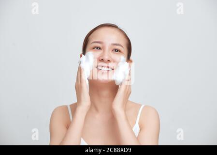Glücklich attraktive junge asiatische Frau Anwendung schäumende Reinigungsmittel auf ihr Gesicht über weißem Hintergrund. Stockfoto