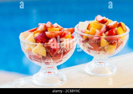 Zwei Schüsseln frischen Obstsalat mit Schwimmbad im Hintergrund. Konzept der gesunden Ernährung, Antioxidantien und Sommerzeit. Stockfoto