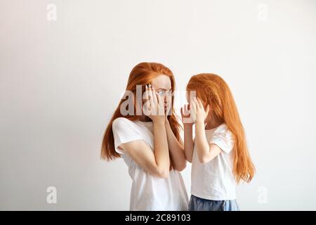 Schöne junge Mutter mit langen losen roten Haaren Grimassen beim Posieren mit ihrem niedlichen kleinen 4 Jahre alten Mädchen, einander zu suchen, was pockerig Gesicht ein Stockfoto