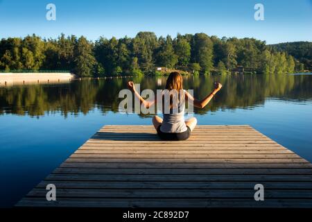 Junge Frau auf Holzponton oder Pier Yoga üben & entspannen im Urlaub. Stockfoto