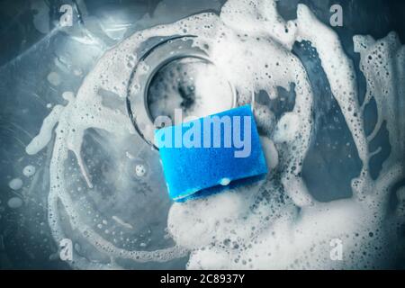 In der Küchenspüle befindet sich ein blauer Schwamm zum Spülen, der mit Seife zum Waschen des Spülbeckens verwendet wurde. Hausarbeit. Stockfoto