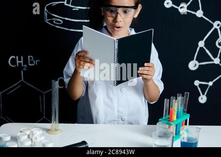 Kleine süße Mädchen in weißen Wissenschaftler Mantel Lesesteine, stehen im Schullabor, Gefühl Überraschung, Aufregung und Freude mit Ergebnissen des Experiments. Stockfoto