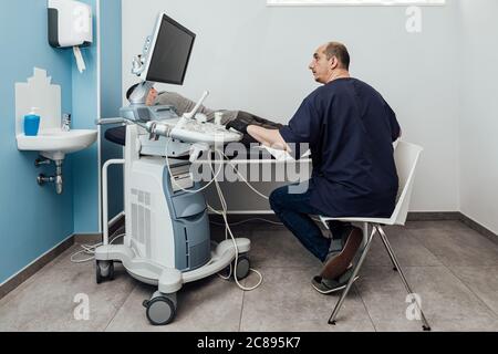 Arzt, der einen Ultraschalluntersuchung an einem Patienten durchführt, der auf einer Bahre liegt Stockfoto